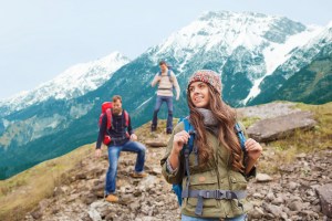adventure, travel, tourism, hike and people concept - group of smiling friends with backpacks walking down downhill over mountains background